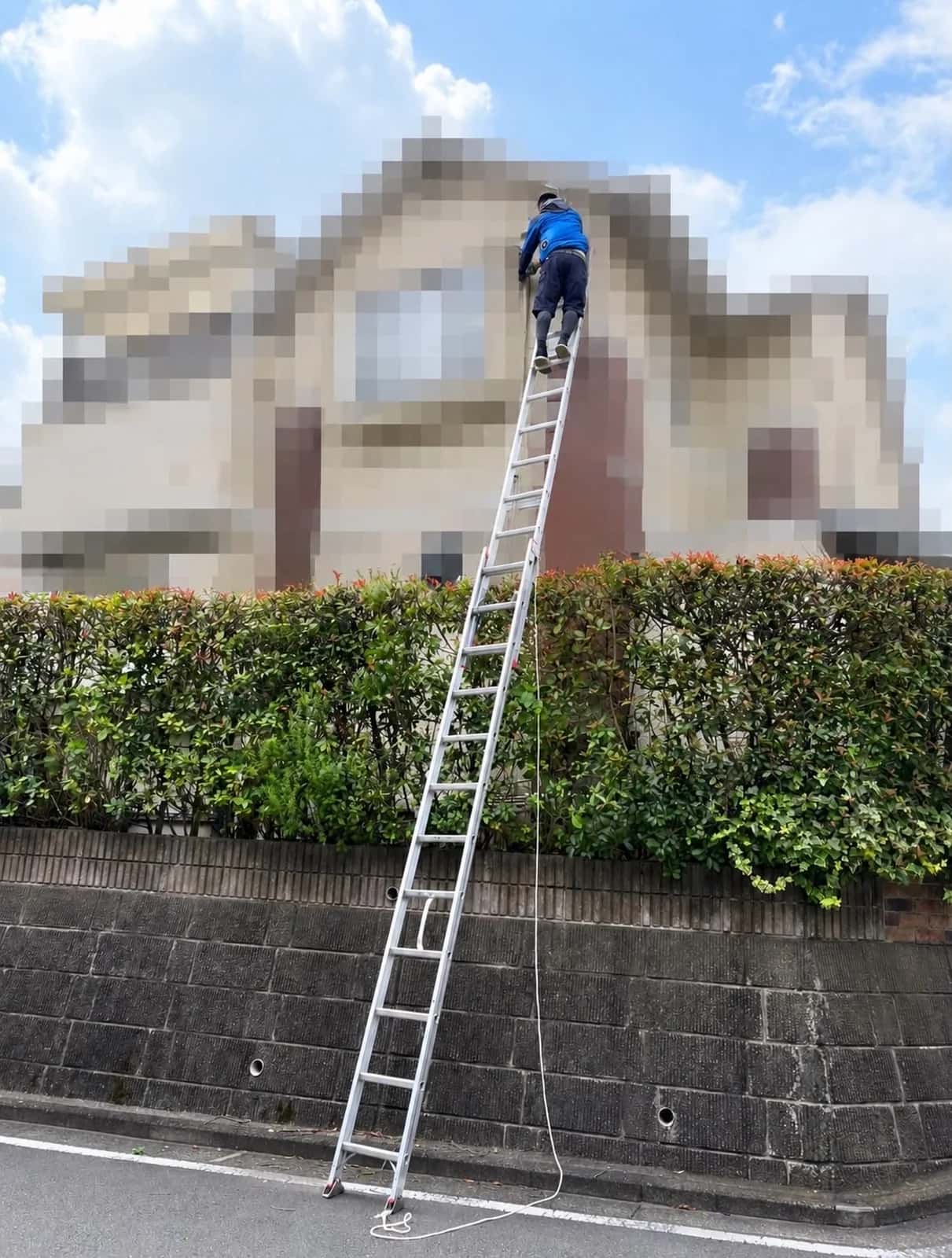 住宅の外壁に長いはしごを掛け、高い位置で作業するスタッフ