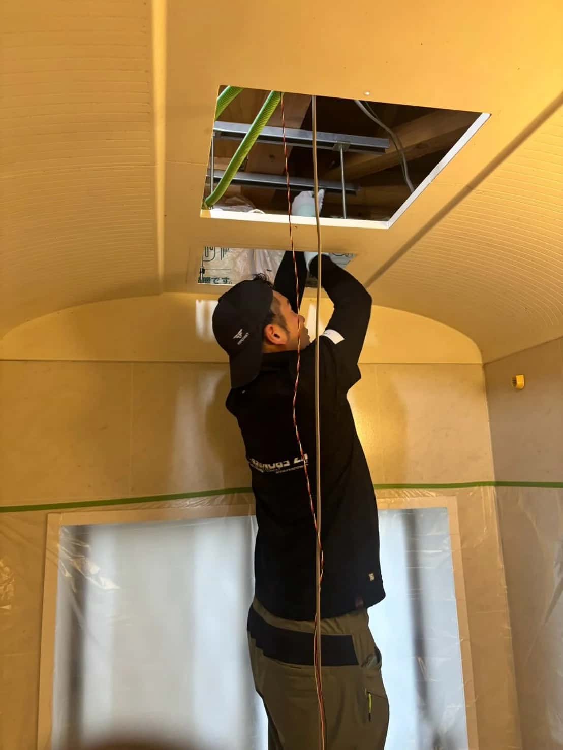 養生した浴室で、天井の点検口から作業するスタッフ