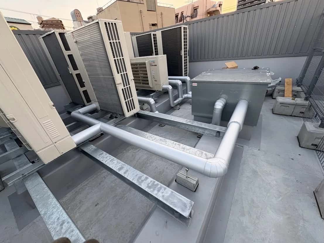 屋外の室外機につながる空調配管に、銀色のラッキングカバーを施工した様子